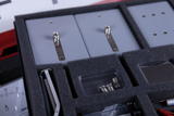 Ein Physik-Experimentierkasten enthält verschiedene graue Module und Zubehör in einer Schaumstoffeinlage. Sichtbar sind unter anderem zwei Metallkontakte sowie Ersatzleuchtmittel in einer kleinen Kunststoffbox.