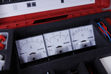 Drei analoge Messgeräte für Stromstärke und Spannung liegen in einem roten Transportkoffer mit Schaumstoffeinlage. Die Geräte dienen als Lehrmaterial für physikalische Experimente im Bildungsbereich.