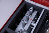 Ein roter Koffer enthält verschiedene metallene Präzisionsbauteile und Halterungen, die sicher in Schaumstoff eingebettet sind. Die Anordnung deutet auf ein wissenschaftliches Experimentierset aus Aluminium hin.