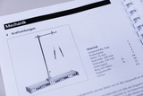 Ein Lehrbuchblatt zum Thema Mechanik zeigt eine schematische Zeichnung eines physikalischen Versuchsaufbaus zu Kraftwirkungen. Daneben ist eine detaillierte Materialliste mit Komponenten wie Stativstäben und einer Profilschiene aufgeführt.